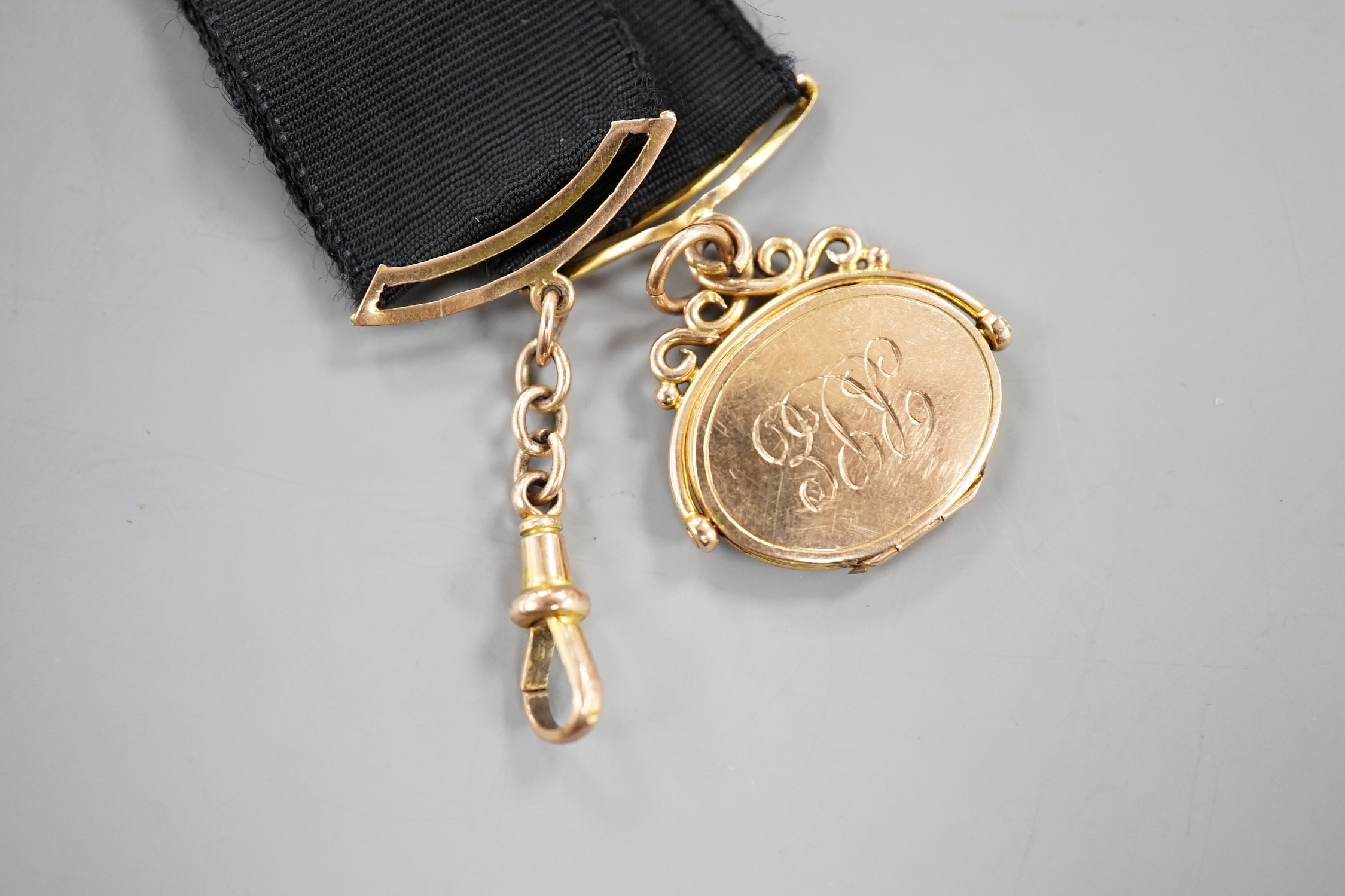 A Victorian yellow metal oval locket fob, hung from a yellow metal mounted black suspension sash, with later engraved date and initials.